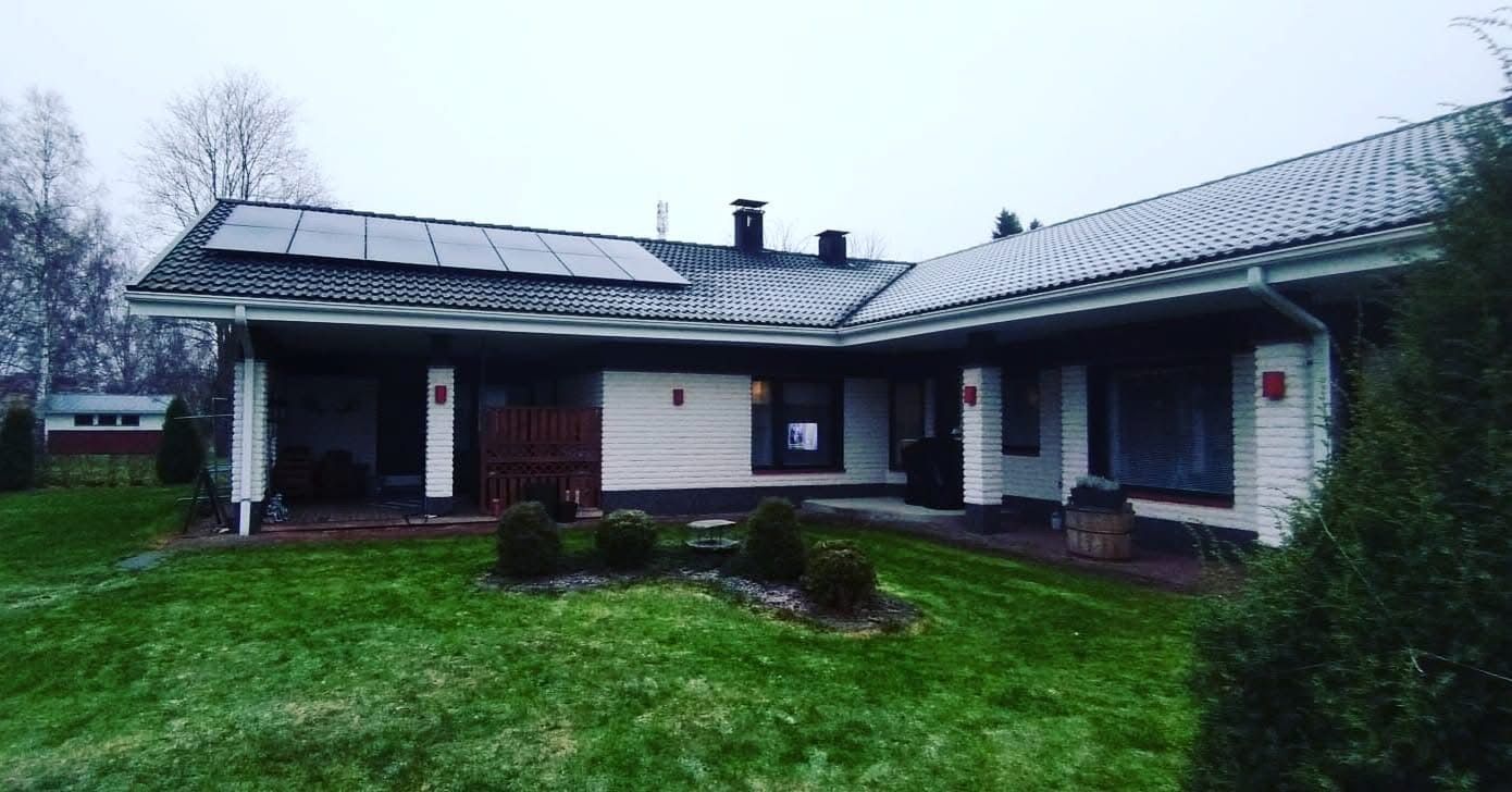 Yksikerroksinen tiilitalo, jossa on tumma katto ja aurinkopaneelit, etupiha ja katettu kuisti