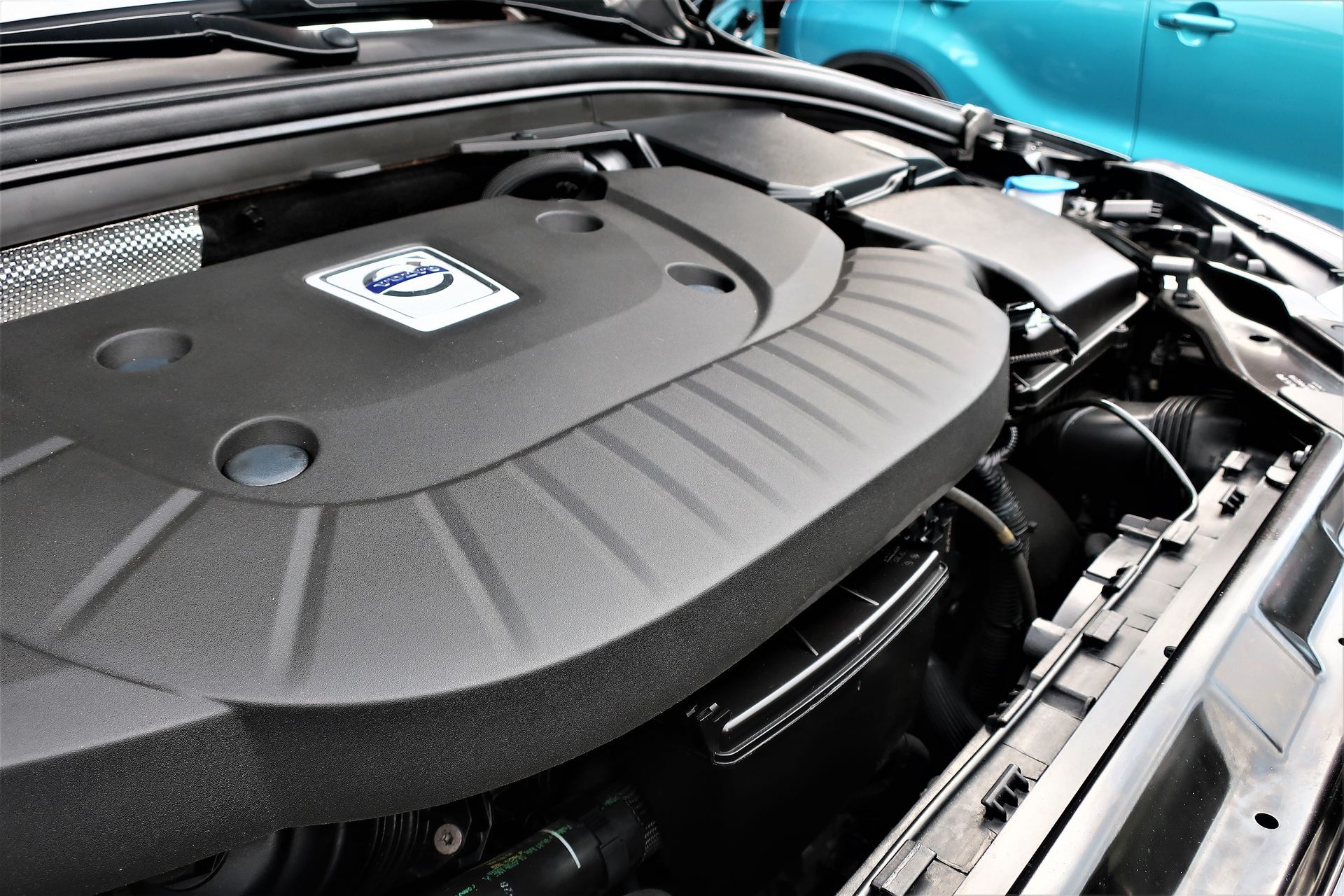 Nahaufnahme eines Volvo-Motorraums mit schwarzer Motorabdeckung und blauem Karosserieteil
