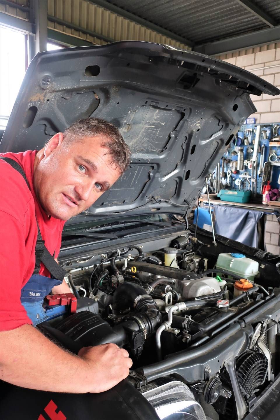 Ein Mechaniker beugt sich in einer Werkstatt über den Motorraum eines Autos mit geöffneter Motorhaube.