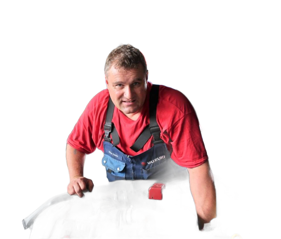Ein Mechaniker in rotem Hemd und Overall arbeitet in einer Garage unter der Motorhaube eines Autos.