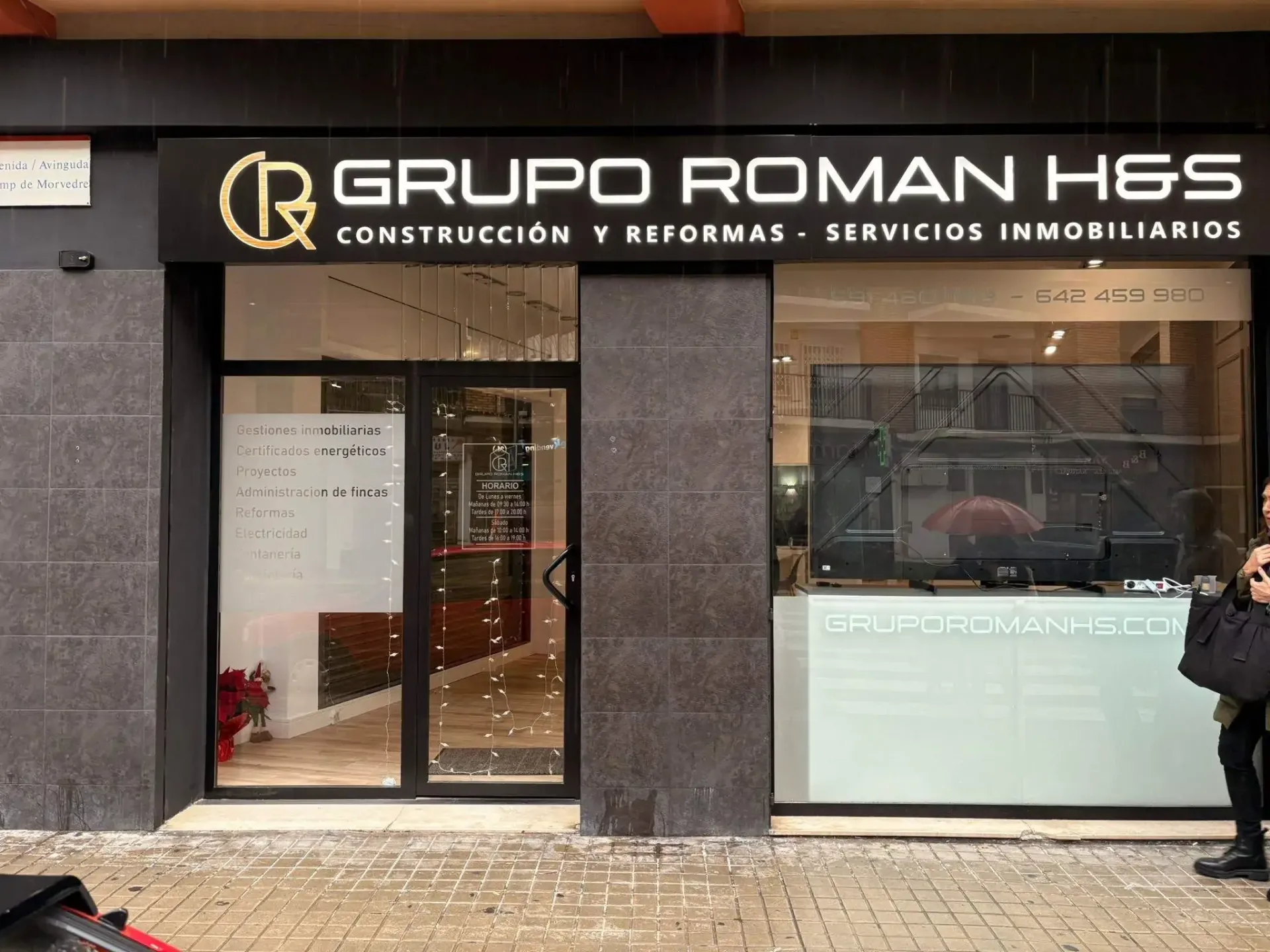 Local comercial de “Grupo Roman AHS” con entrada de cristal y escaparate en una esquina.