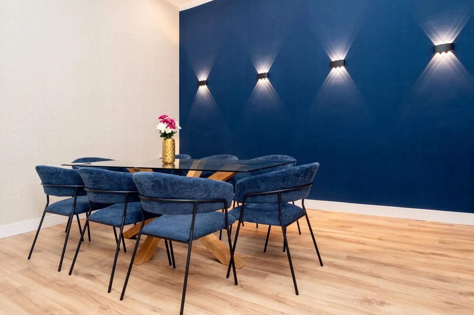 Comedor moderno con una pared decorativa de color azul oscuro, sillas azules y una mesa con un centro de mesa floral.