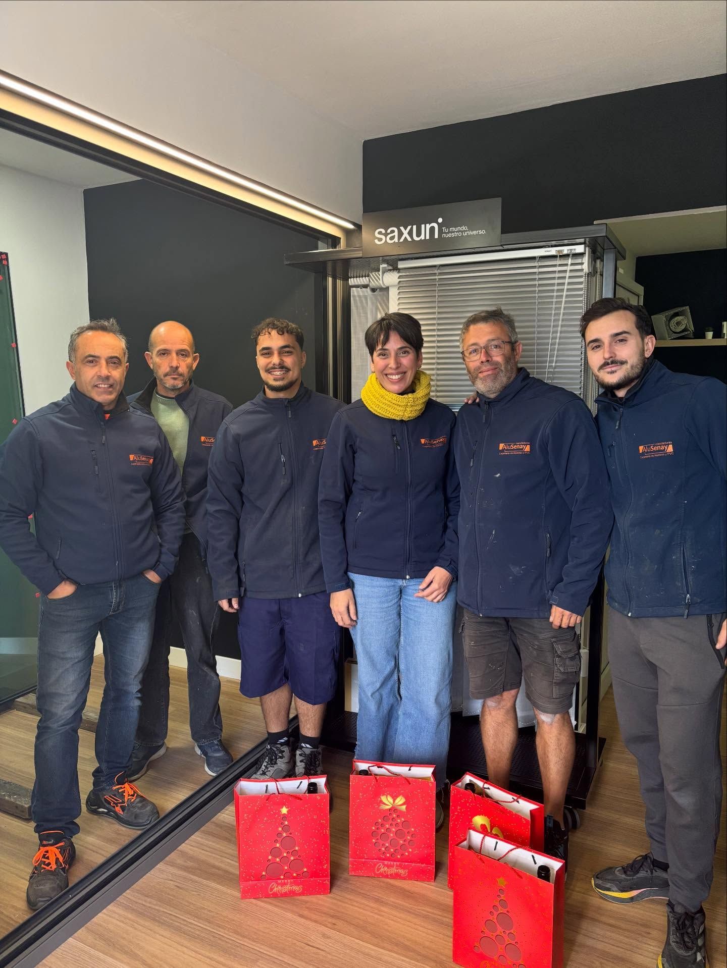 Seis personas con chaquetas azul marino a juego posan en una sala de exposiciones de una oficina, sosteniendo bolsas rojas