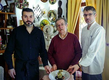 Tres hombres están de pie uno al lado del otro frente a un plato de comida.