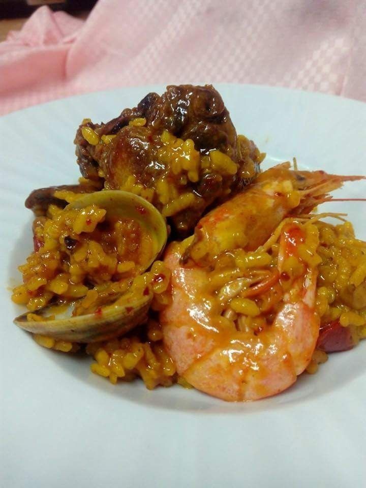 Un plato blanco cubierto con camarones, almejas y arroz.