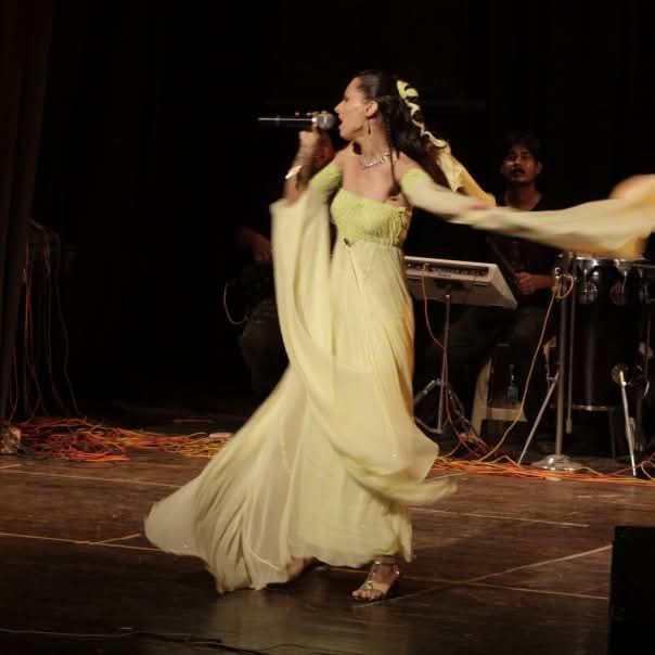 Una mujer con un vestido amarillo cantando en un micrófono.
