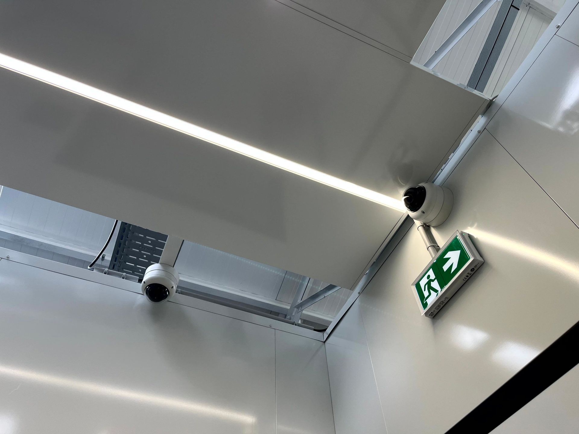 Plafond avec des luminaires linéaires, des grilles de ventilation et un panneau de sortie vert dans un intérieur moderne.