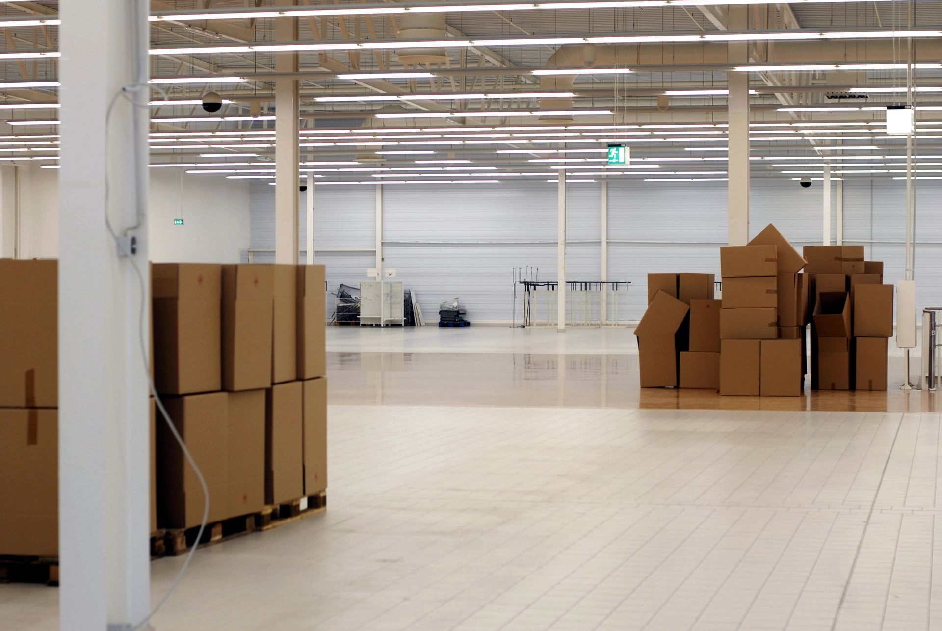 Entrepôt vide avec des cartons empilés sur des palettes, sous un éclairage zénithal puissant