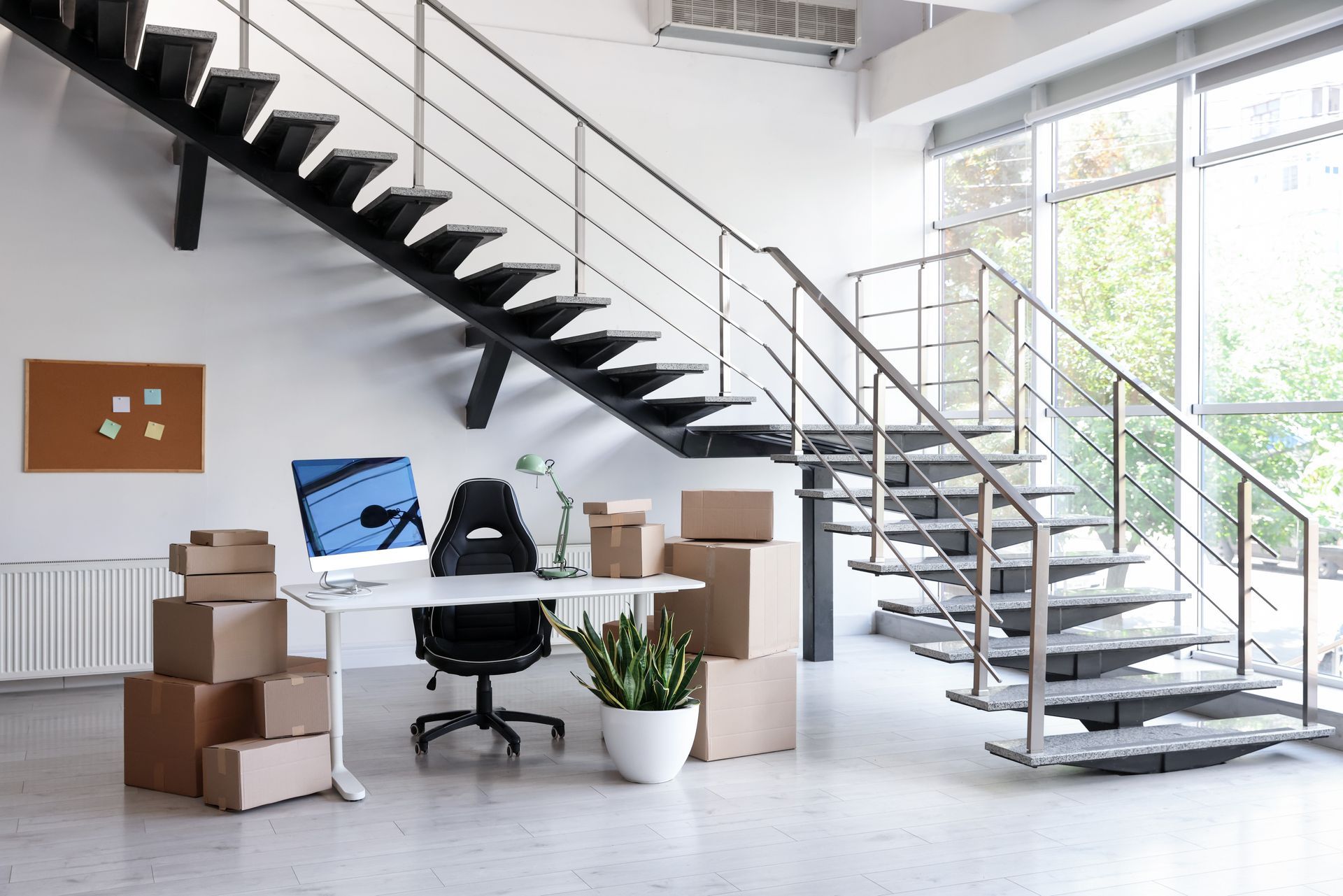 Bureau moderne avec escalier, cartons de déménagement, bureau et plante en pot dans un espace de travail ouvert et lumineux