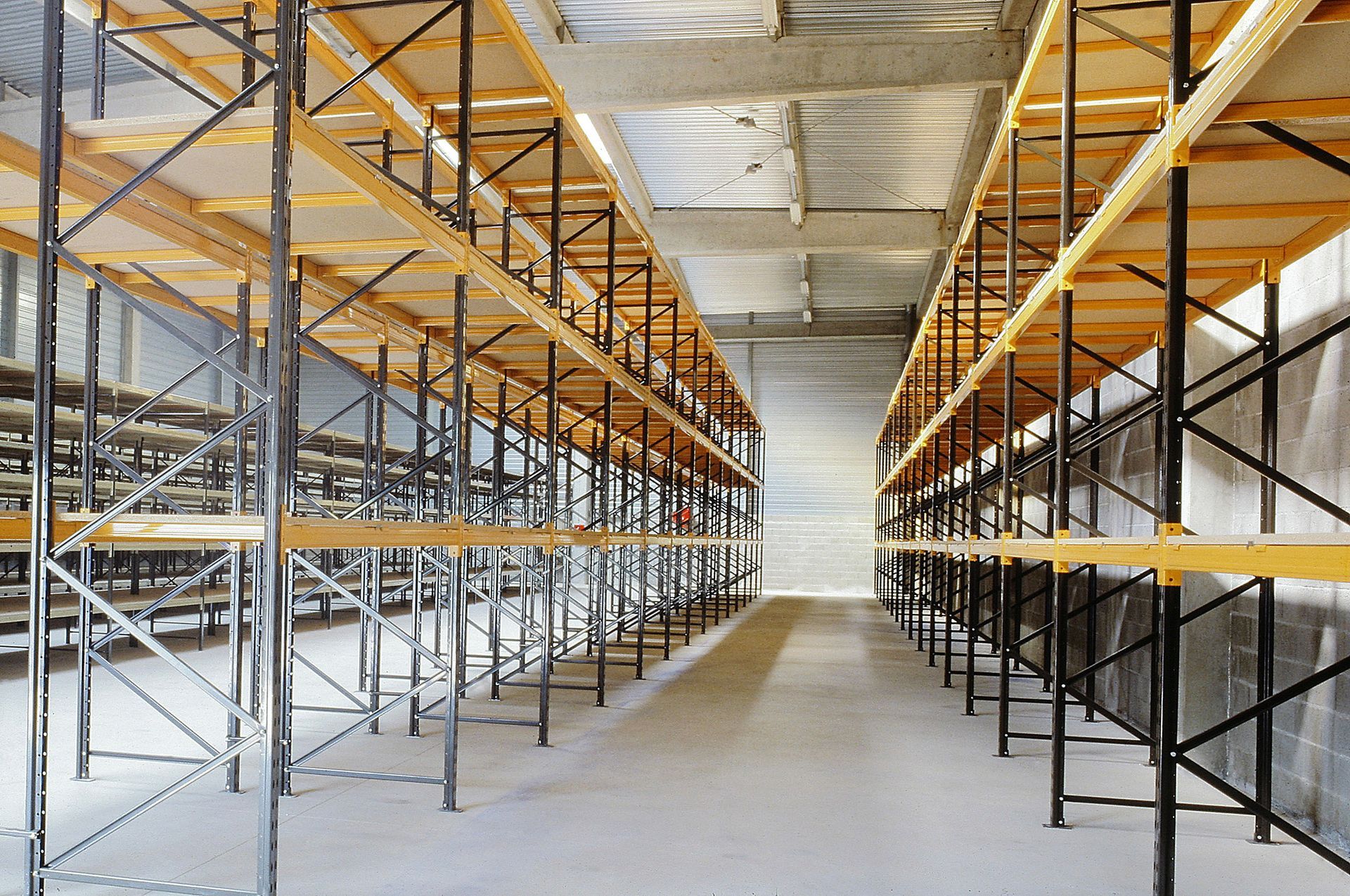 Allée d’entrepôt vide avec des rayonnages métalliques et des étagères en bois sous un éclairage industriel vif