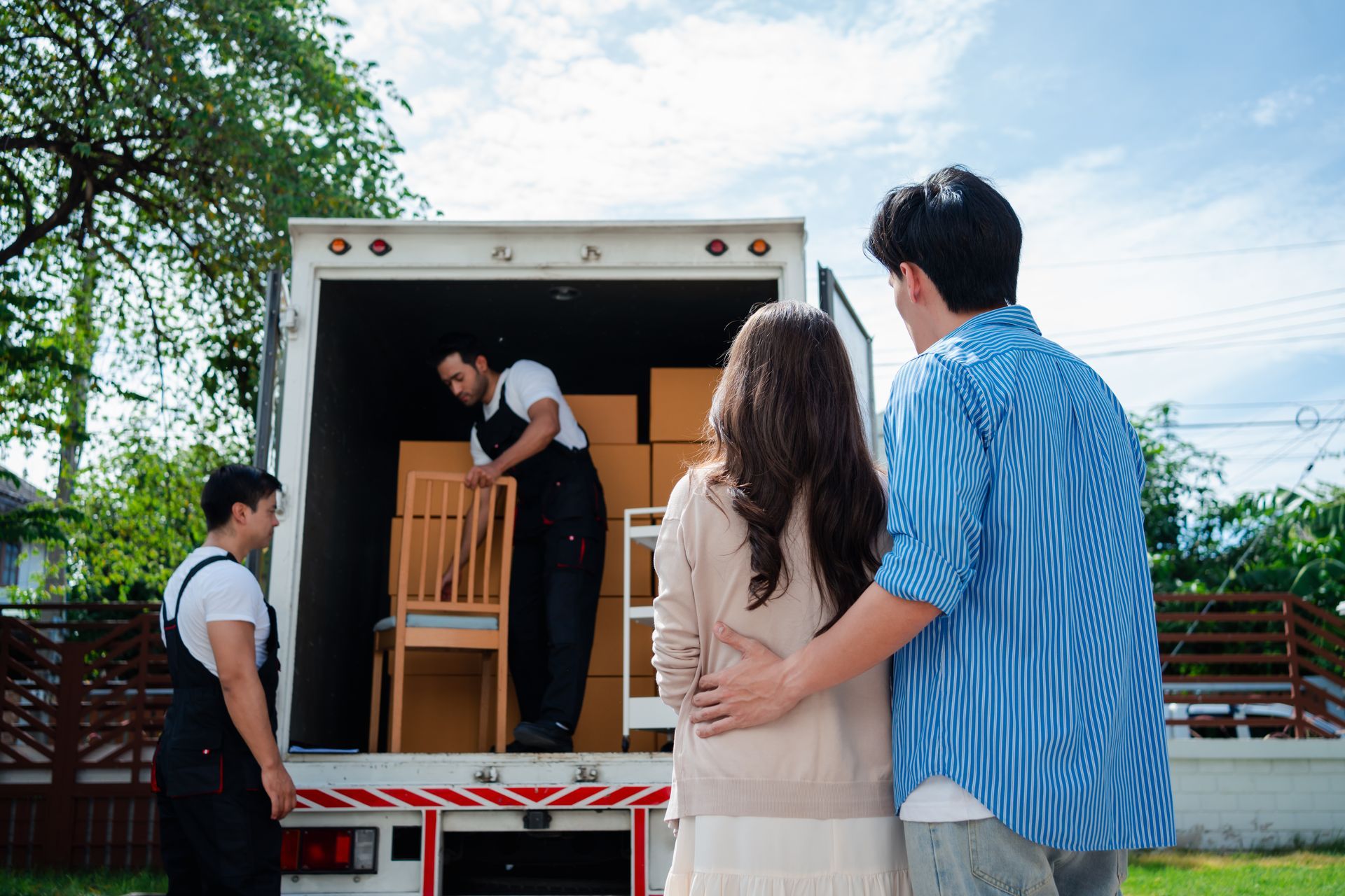 Des personnes déchargent des chaises en bois et des cartons d’un camion en plein air