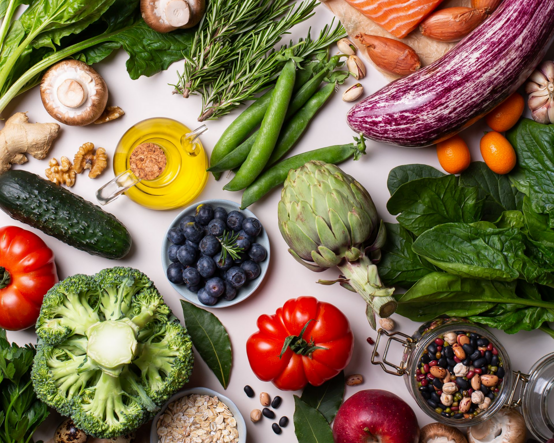 Vue de dessus de légumes frais et colorés, de fruits, de noix, de céréales, d'herbes aromatiques, d'huile d'olive et de saumon disposés sur une surface claire.