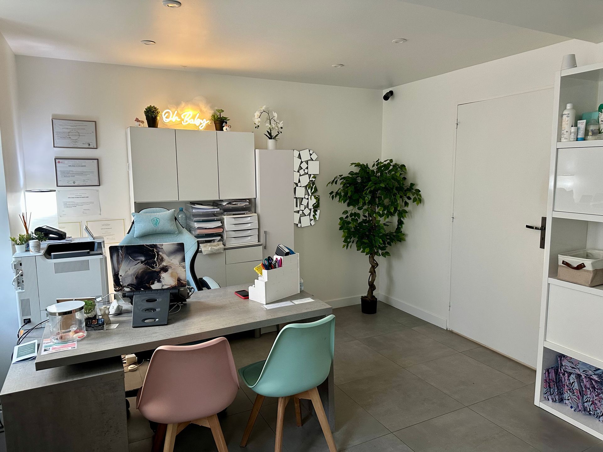 Une femme enceinte vêtue d'un blazer noir est assise en tailleur, les mains posées sur son ventre, dans un portrait de studio en noir et blanc.