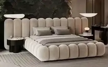 Um quarto moderno com uma cama estofada em tom creme com capitonê, encostada em uma parede de pedra escura e texturizada.