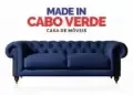 Um sof&aacute; Chesterfield azul com capiton&ecirc; e p&eacute;s de madeira, com a inscri&ccedil;&atilde;o "MADE IN CABO VERDE CASA DE M&Oacute;VEIS".