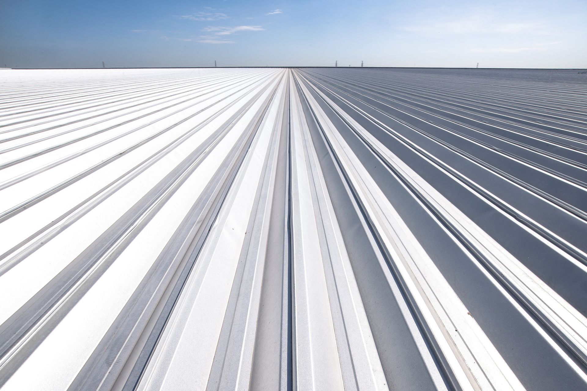 Vista en perspectiva de un largo techo de metal corrugado blanco bajo un cielo azul claro. Las líneas paralelas crean una sensación de profundidad.