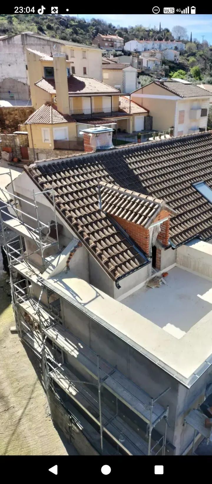 Dos pintores, uno de pie y otro arrodillado, trabajan en el exterior blanco de un edificio. El edificio tiene detalles en rojo y un techo gris.