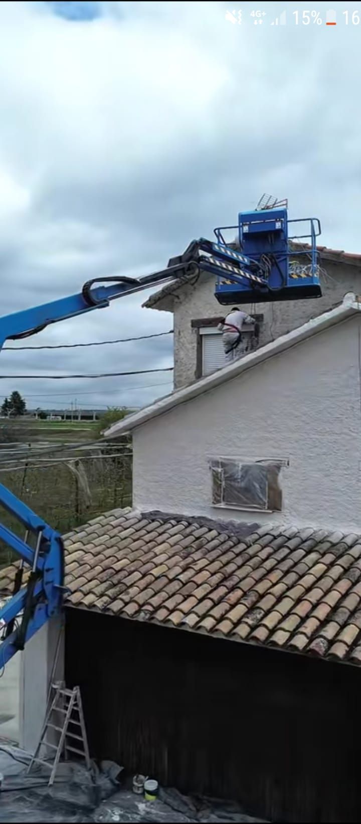 Dos trabajadores de la construcción en un andamio suspendido de color naranja, pintando el exterior blanco de un edificio alto.