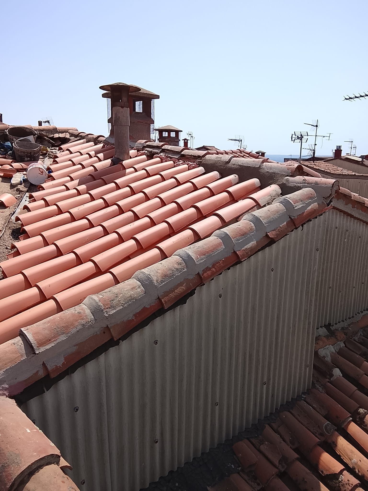 Techador instalando tejas negras en un tejado bajo un cielo brillante.