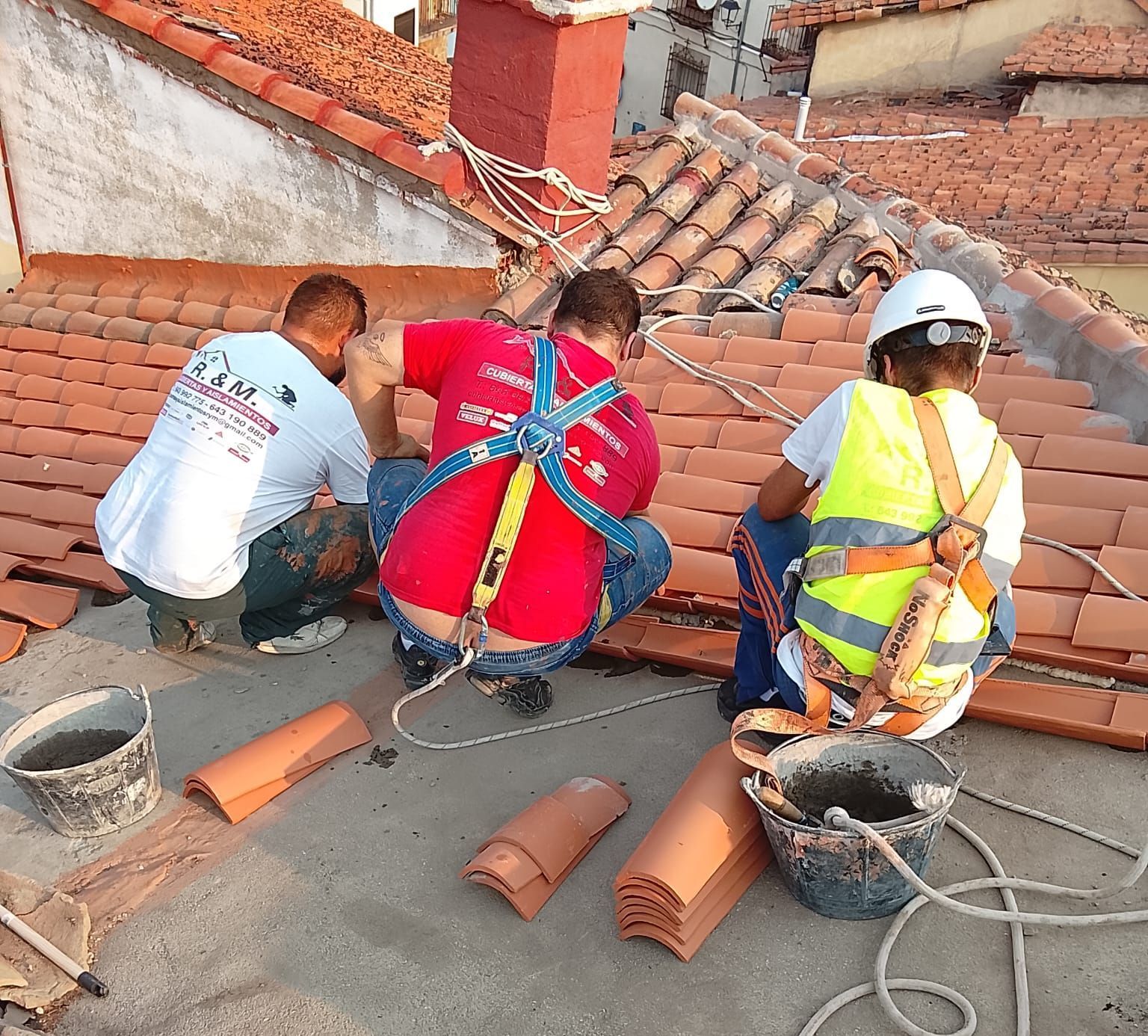 Techador instalando tejas negras en un tejado bajo un cielo brillante.