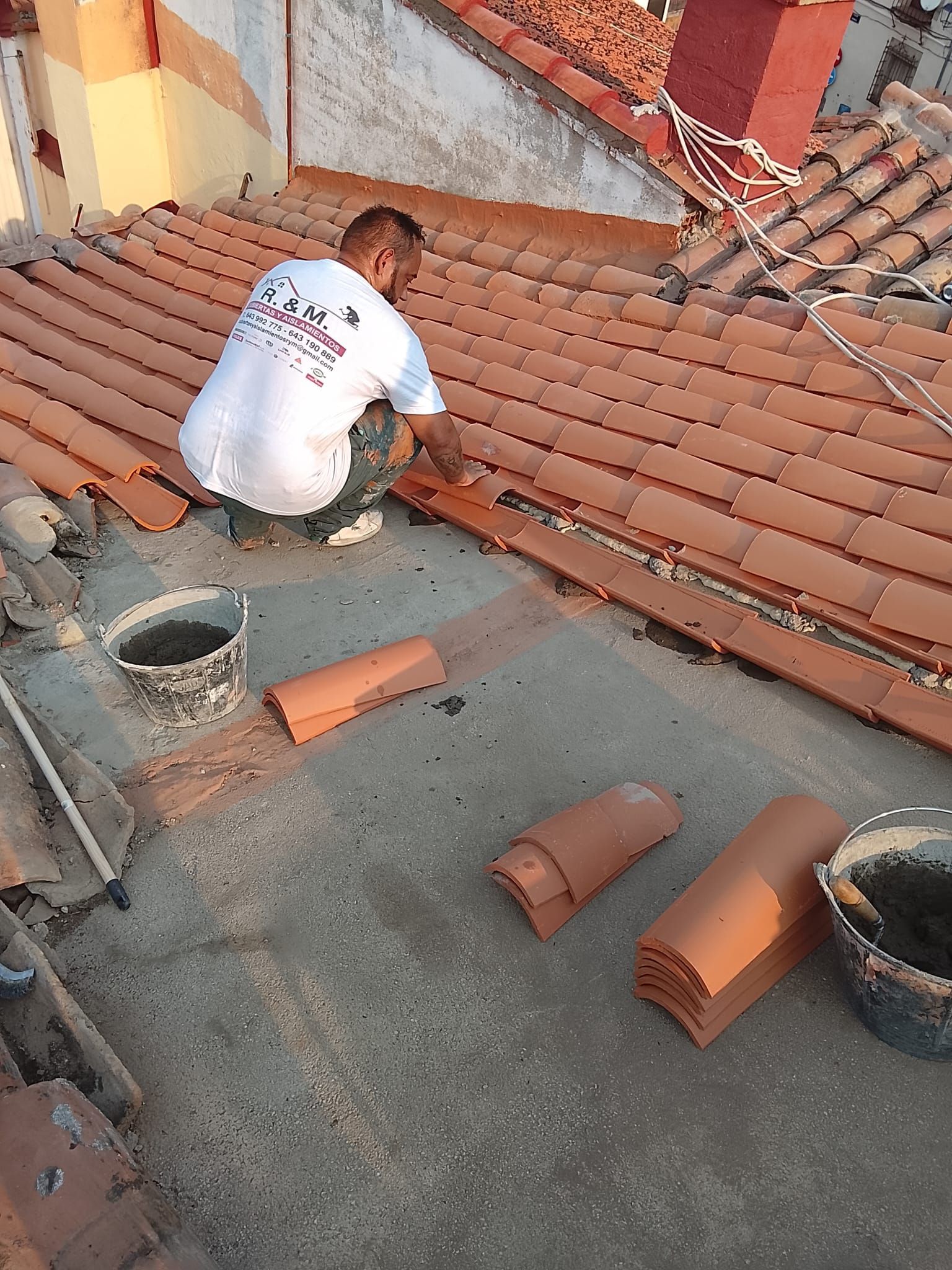 Techador instalando tejas negras en un tejado bajo un cielo brillante.