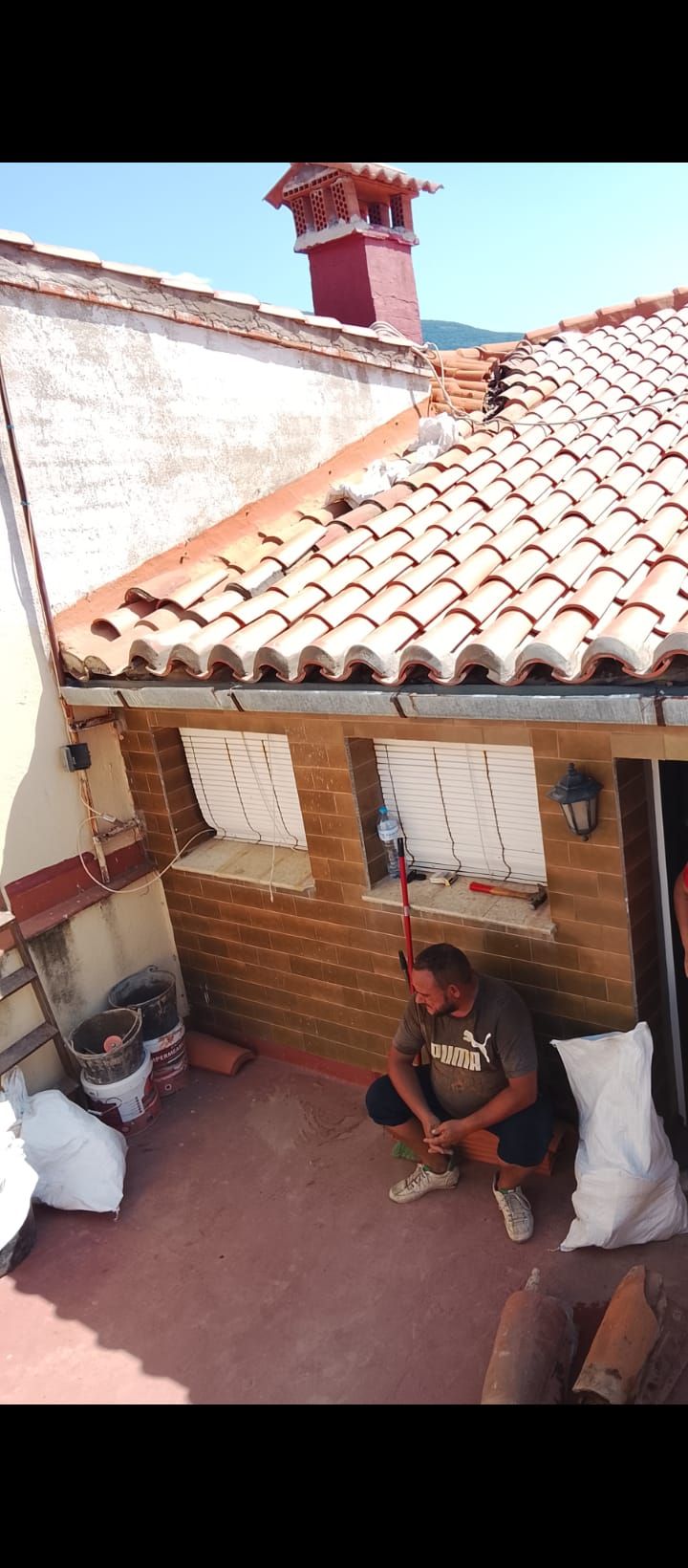 Techador instalando tejas negras en un tejado bajo un cielo brillante.