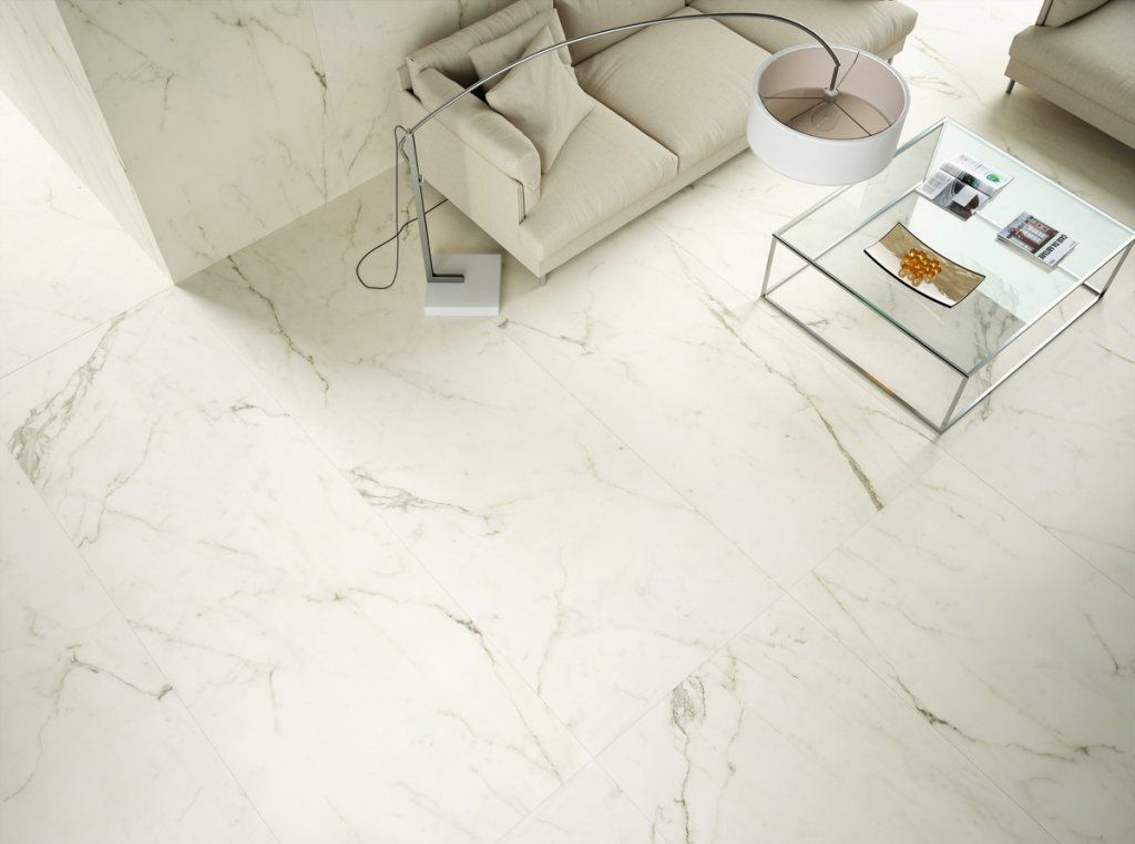 Sala de estar con pisos de mármol crema, un sofá beige, una mesa de vidrio y una lámpara de pie.