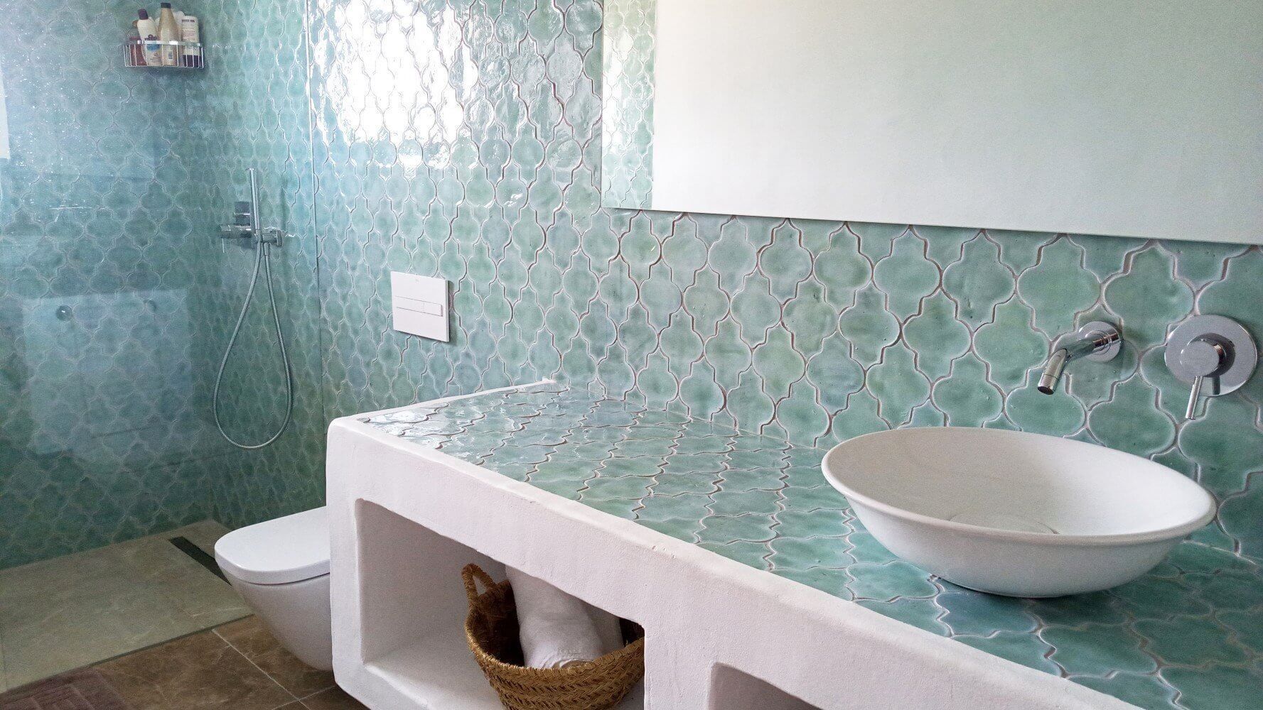 Baño con mosaicos de color verde azulado, lavabo blanco y tocador empotrado.