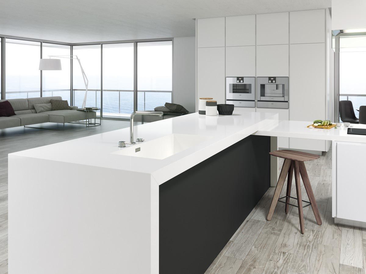 Cocina moderna con encimera blanca y base gris oscuro, junto a un salón con amplios ventanales.