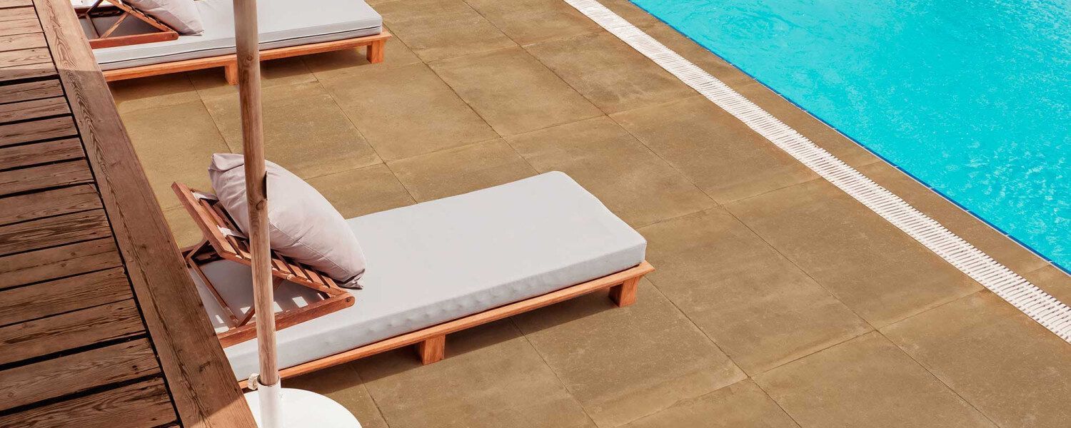 Vista a la piscina con tumbonas, suelo color canela y agua turquesa.