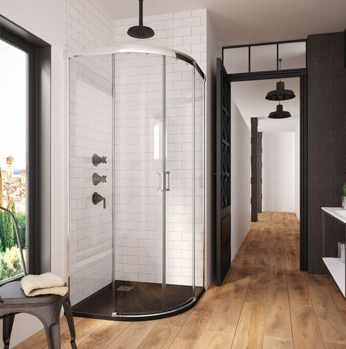 Plato de ducha gris oscuro con desagüe, junto a un panel de vidrio. Azulejos grises y blancos al fondo.