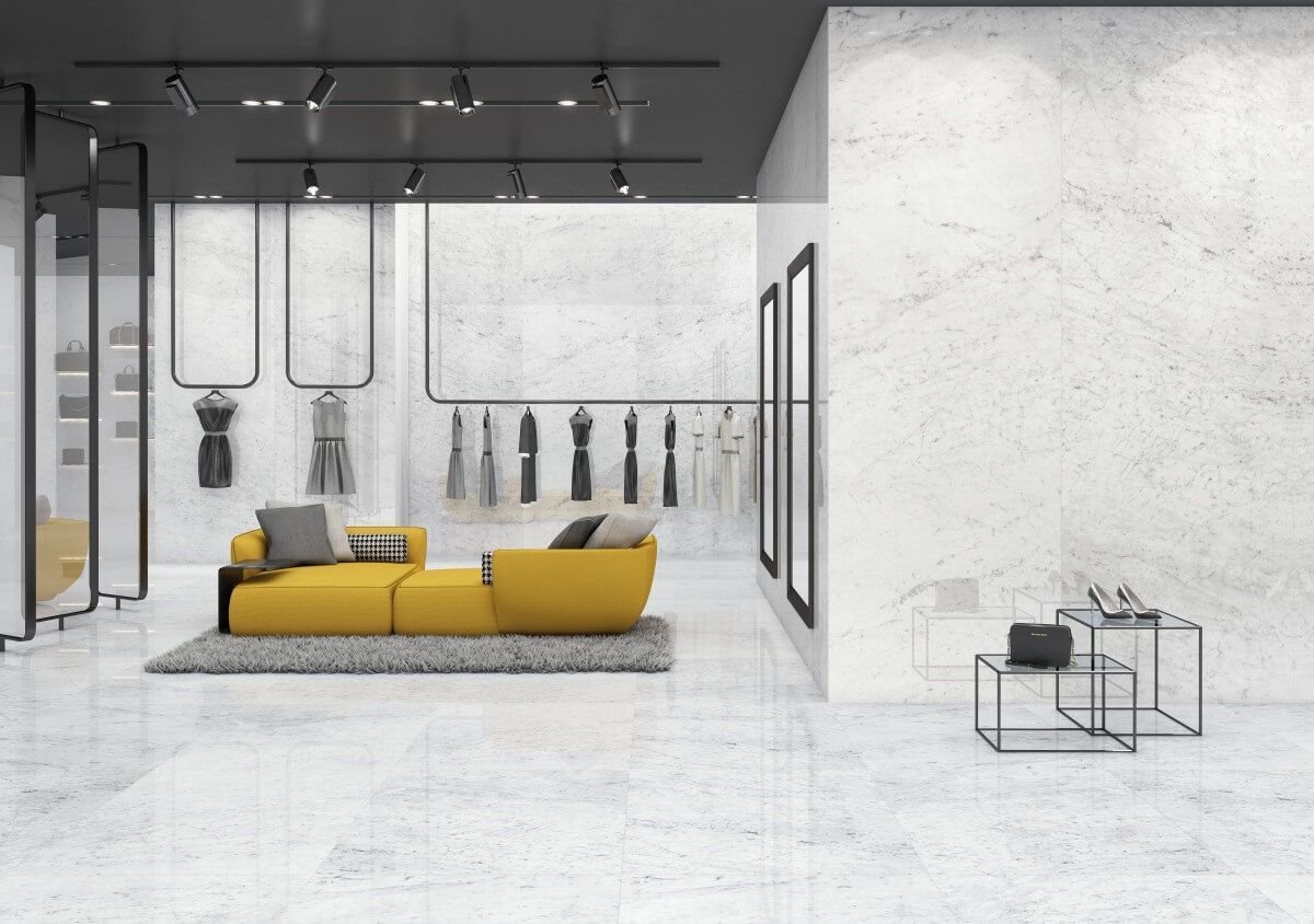 Boutique de moda moderna con sofá amarillo, exhibidores de ropa y paredes blancas.