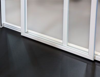 Paneles de vidrio corredizos con marco blanco y vidrio esmerilado, piso negro.