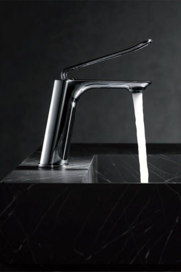 Grifo cromado con chorro de agua, montado sobre mármol negro, fondo oscuro.