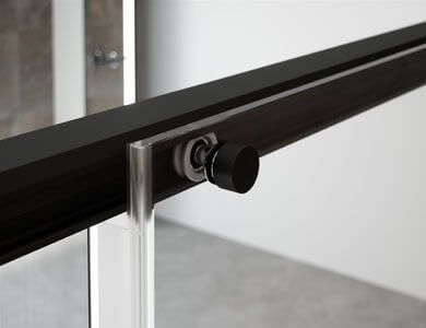 Manija cromada para puerta de ducha sobre panel de vidrio. Fondo gris, base de ducha blanca.