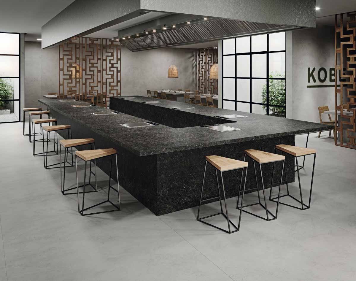 Un restaurante moderno con un gran mostrador negro, taburetes de madera y una pared decorativa.