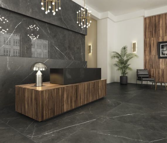 Área de recepción con paredes y piso de mármol oscuro, escritorio de madera y planta de interior.