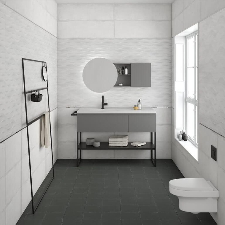 Baño moderno con paredes blancas, tocador gris, espejo redondo y pisos de baldosas negras.