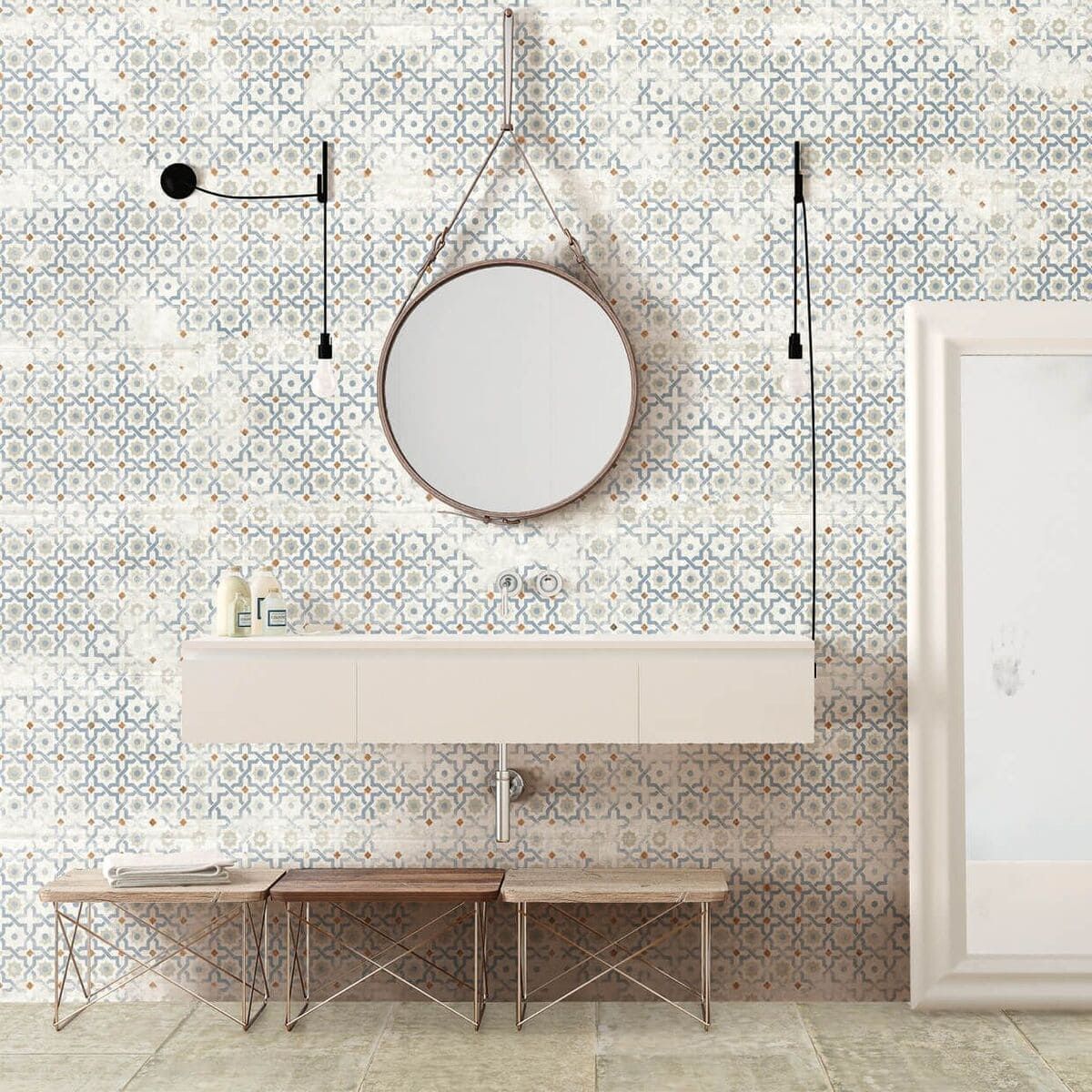 Baño con azulejos estampados en azul y blanco, tocador flotante, espejo redondo y dos bancos pequeños.