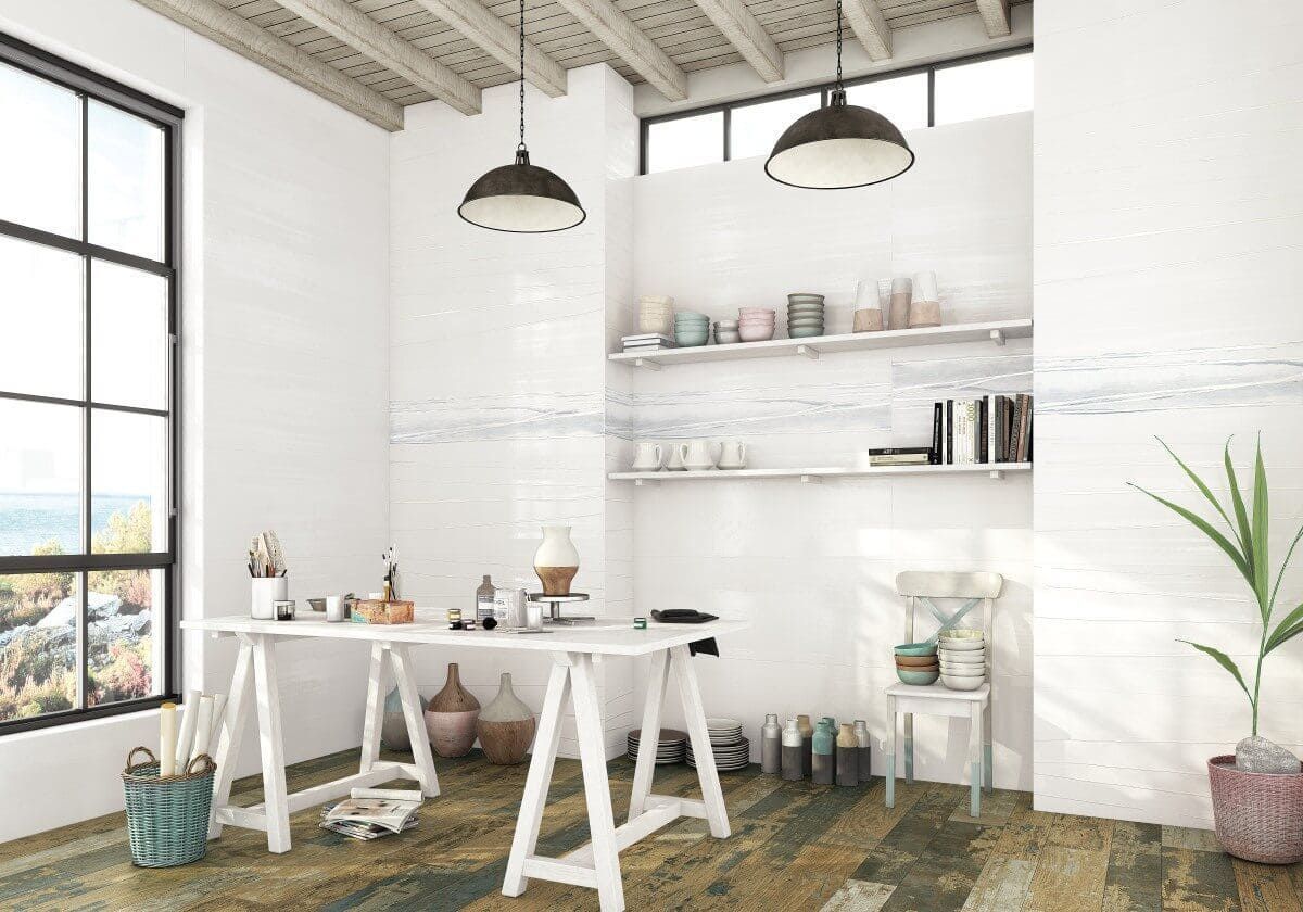 Luminoso estudio de arte con un gran ventanal, paredes blancas y suelo de madera. Una mesa blanca contiene materiales de arte.