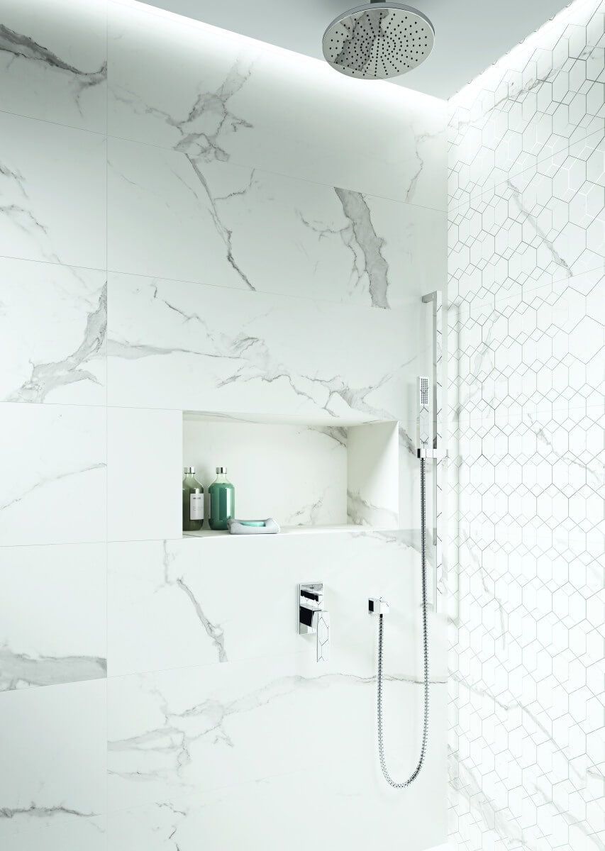 Ducha con azulejos de mármol blanco con estante incorporado para guardar artículos de tocador, cabezal de ducha plateado y ducha de mano.
