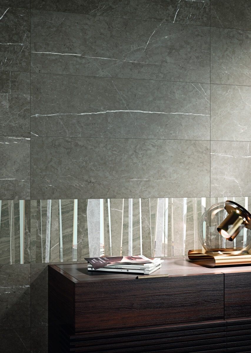 Pared de azulejos gris oscuro con detalles blancos horizontales y verticales, tocador de madera oscura.