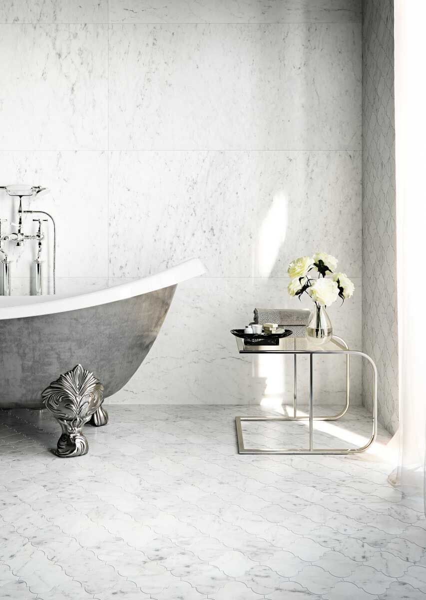 Elegante baño gris con bañera con patas, mesa pequeña con flores y pisos de mármol.