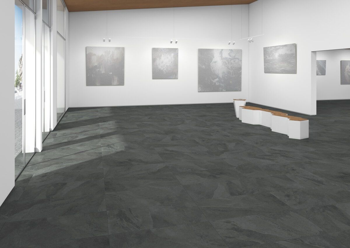 Interior de galería de arte con pinturas abstractas grises, bancos blancos y piso de textura oscura.