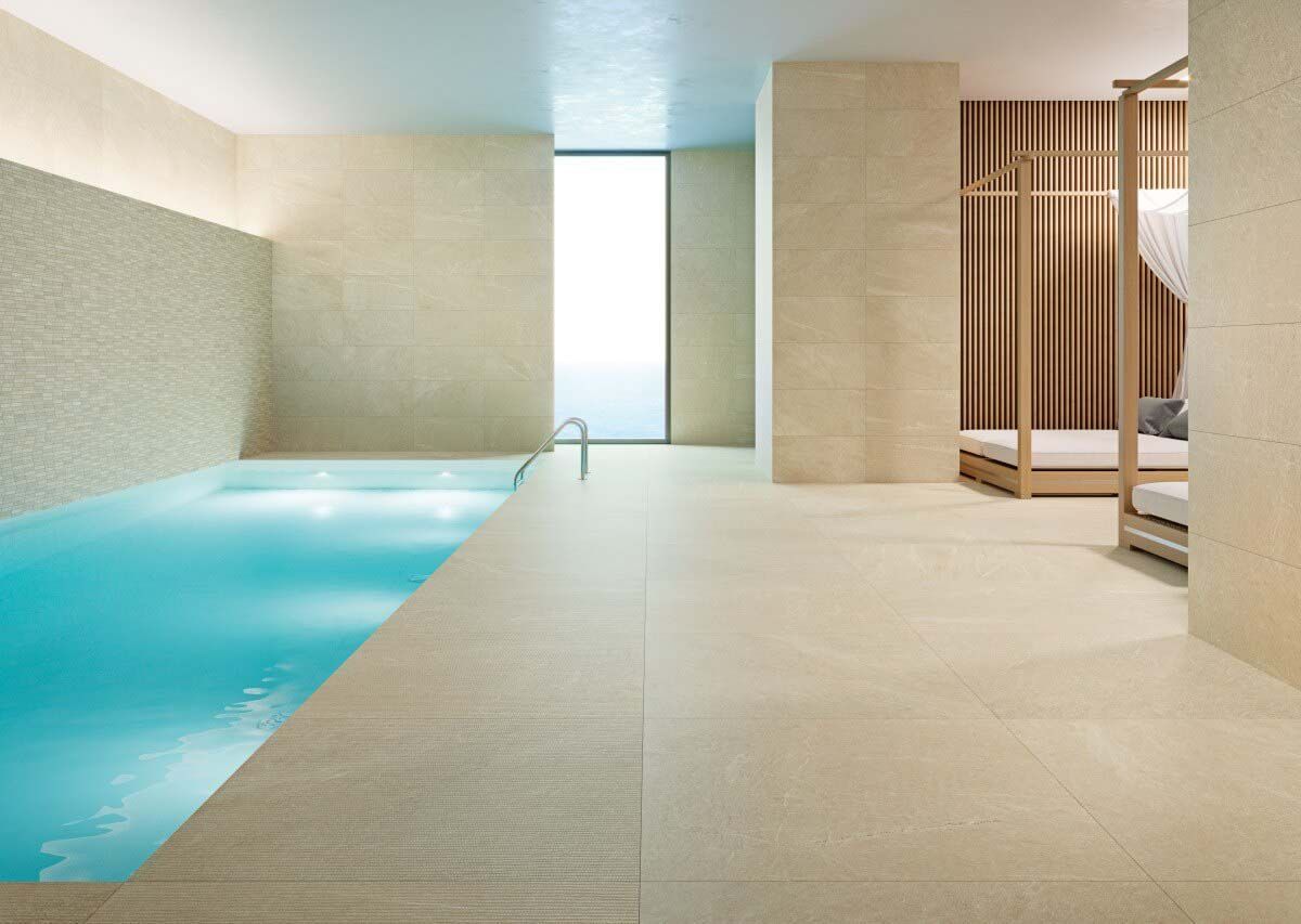 Spa interior con piscina y tumbonas. Paredes y suelos en tonos beige suave y luz natural.