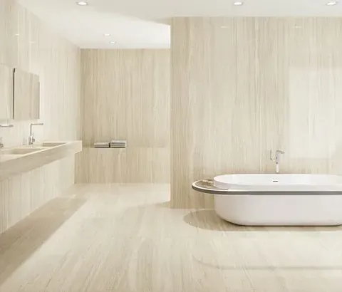 Amplio baño con paredes y suelo de azulejos beige. Una bañera blanca se encuentra junto a un gran ventanal.