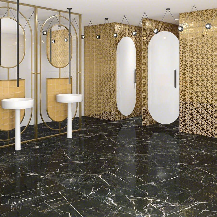 Baño de lujo con piso de mármol negro, detalles dorados y espejos y cabinas de forma ovalada.