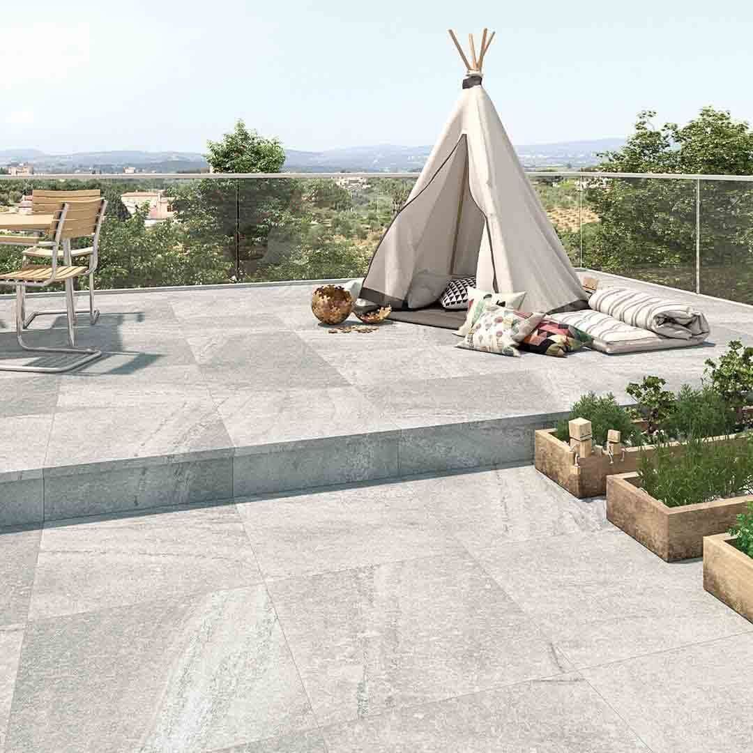 Patio al aire libre con baldosas de piedra gris claro, tipi, asientos y jardineras.