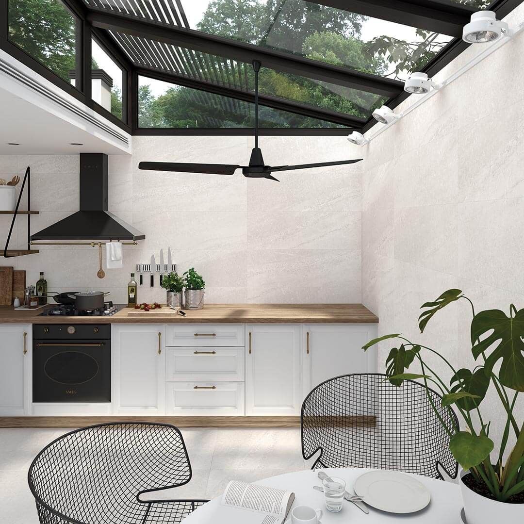 Cocina luminosa con gabinetes blancos, encimera de madera, campana extractora negra, techo de vidrio y ventilador.