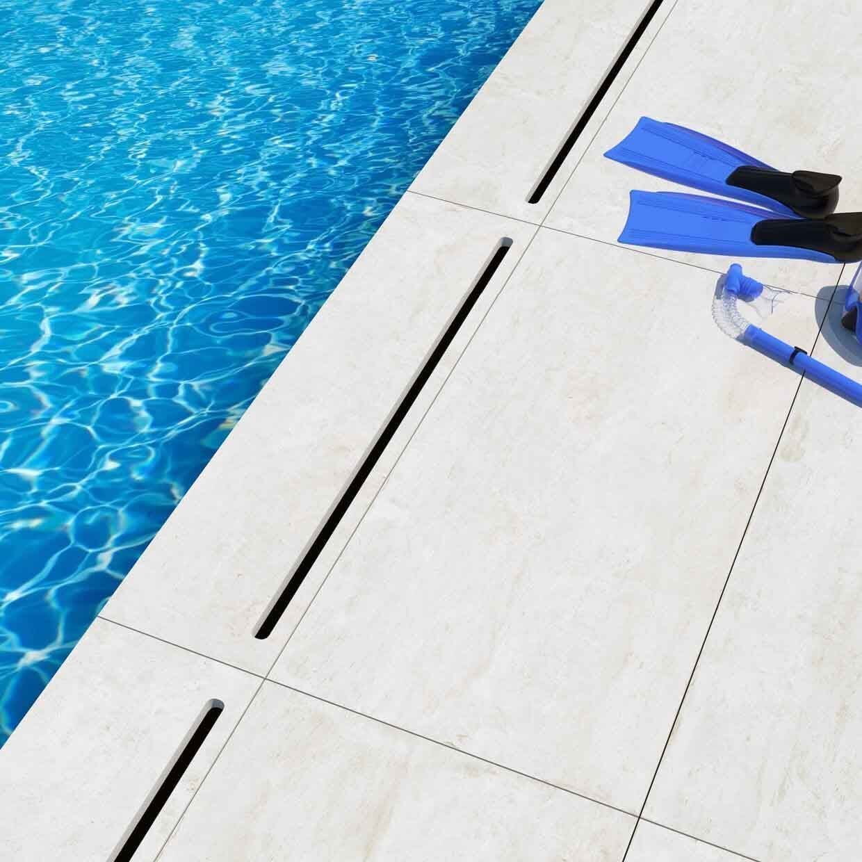 Piscina con agua azul y equipo de buceo: aletas, tubo y máscara. Azulejos blancos con rejillas de drenaje oscuras.